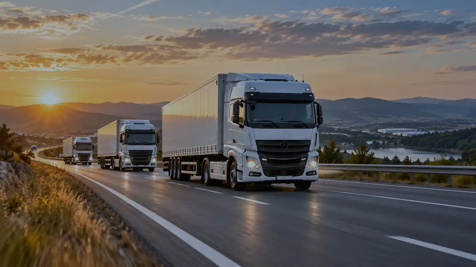 Tre autoarticolati in marcia su un’autostrada al tramonto, fra colline.
